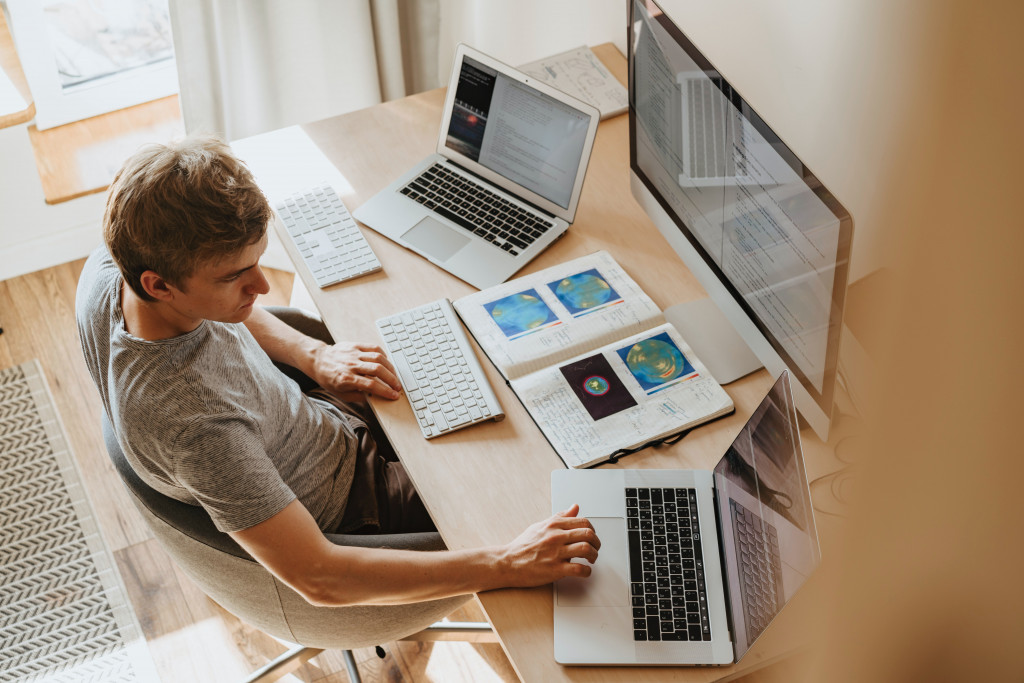 Mann arbeitet an drei Computern gleichzeitg